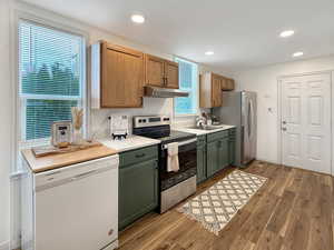 Kitchen featuring sink, light hardwood / wood-style flooring, green cabinets, appliances with stainless steel finishes, and a textured ceiling