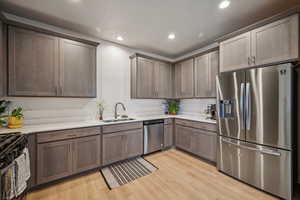 Kitchen with sink, stainless steel appliances, light wood-style floors, grey cabinetry, and white quarts countertops.