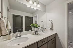 Primary bathroom featuring a tile shower, white quarts countertop with two sinks, a grey wood vanity, and connection to the primary closet