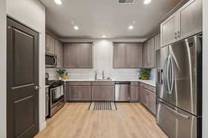 Kitchen with sink, light wood-style flooring, stainless steel appliances, white quarts countertops and gray wood cabinets