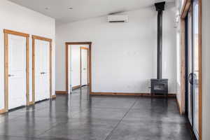 Unfurnished bedroom featuring a towering ceiling, a wood stove, and a wall mounted AC