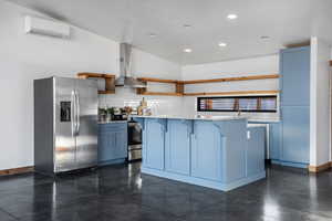 Kitchen featuring a kitchen breakfast bar, wall chimney exhaust hood, a center island, an AC wall unit, and stainless steel appliances