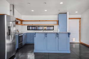 Kitchen featuring stainless steel appliances, a center island, blue cabinetry, and a kitchen bar