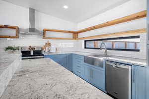 Kitchen with sink, stainless steel appliances, light stone countertops, and wall chimney exhaust hood