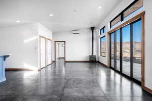 Unfurnished room featuring lofted ceiling, a wall unit AC, and a wood stove