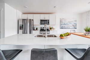 Kitchen with white cabinets, stainless steel appliances, a kitchen bar, and an island with sink