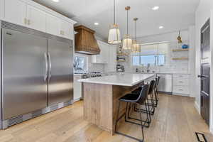 Kitchen with premium range hood, white cabinetry, appliances with stainless steel finishes, and a center island