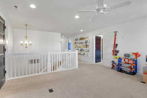 Interior space featuring built in shelves, ceiling fan with notable chandelier, and light colored carpet