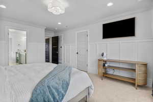 Bedroom with light colored carpet, connected bathroom, and ornamental molding