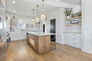 Kitchen featuring white cabinets, a center island, tasteful backsplash, light hardwood / wood-style floors, and hanging light fixtures