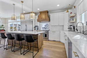 Kitchen featuring sink, premium range hood, white cabinets, light stone counters, and stainless steel appliances