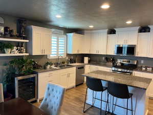 Kitchen featuring appliances with stainless steel finishes, white cabinetry, sink, a kitchen island, and wine cooler