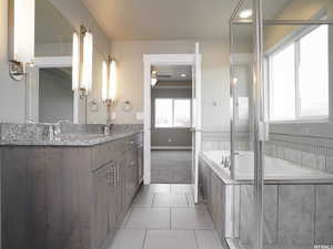 Bathroom featuring a relaxing tiled tub, vanity, and tile patterned flooring