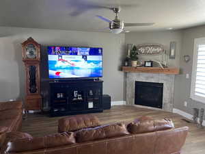 Living room with a tiled fireplace, hardwood / wood-style flooring, a textured ceiling, and ceiling fan