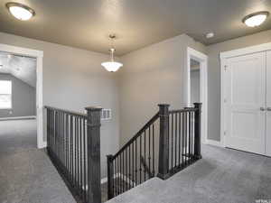 Hall featuring vaulted ceiling, dark colored carpet, and a textured ceiling