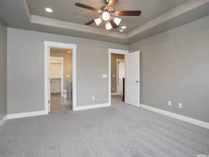 Unfurnished bedroom with ceiling fan, a raised ceiling, light colored carpet, a walk in closet, and a closet