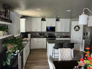 Kitchen featuring a center island, sink, white cabinets, dark wood-type flooring, and stainless steel appliances