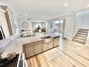 Kitchen with stainless steel dishwasher, light hardwood / wood-style flooring, sink, light stone counters, and stove