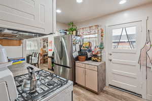 Kitchen with gas range gas stove, white cabinetry, stainless steel fridge, and light hardwood / wood-style flooring