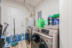 Laundry room featuring electric panel, gas water heater, hardwood / wood-style floors, and independent washer and dryer