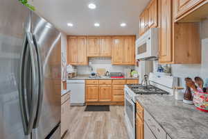 Kitchen featuring light brown cabinets, sink, light wood-type flooring, light stone counters, and white appliances