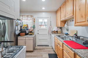 Kitchen with sink, light brown cabinets, light hardwood / wood-style flooring, and stainless steel fridge