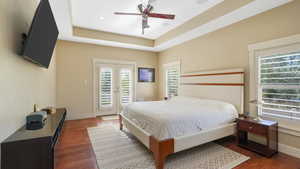 Bedroom featuring access to exterior, dark hardwood / wood-style floors, ceiling fan, and a raised ceiling