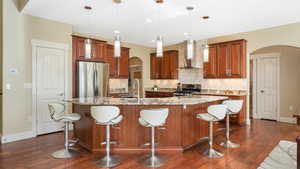 Kitchen featuring pendant lighting, appliances with stainless steel finishes, sink, wall chimney range hood, and an island with sink