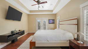 Bedroom with dark hardwood / wood-style flooring, french doors, a raised ceiling, access to outside, and ceiling fan