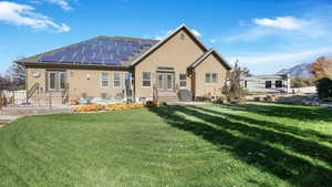 Rear view of house featuring a patio, a lawn, and solar panels