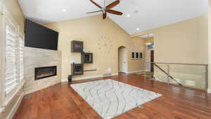 Unfurnished living room with a tile fireplace, dark wood-type flooring, high vaulted ceiling, and ceiling fan