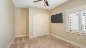 Unfurnished bedroom featuring light colored carpet, a closet, and ceiling fan