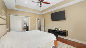 Bedroom featuring wood-type flooring, a raised ceiling, ceiling fan, and a barn door