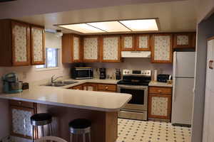 Kitchen featuring kitchen peninsula, sink, white refrigerator, electric stove, and a kitchen bar