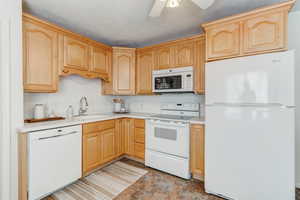 Kitchen with white appliances, light brown cabinetry, sink, backsplash, and ceiling fan