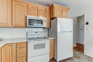 Kitchen with white appliances, tasteful backsplash, and light brown cabinetry