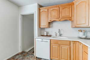 Kitchen featuring sink, white dishwasher, decorative backsplash, and light brown cabinets