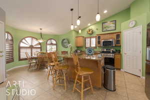 Kitchen featuring light stone countertops, appliances with stainless steel finishes, vaulted ceiling, a breakfast bar area, and light tile patterned flooring