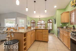 Kitchen featuring light stone countertops, hanging light fixtures, sink, stainless steel appliances, and a center island with sink