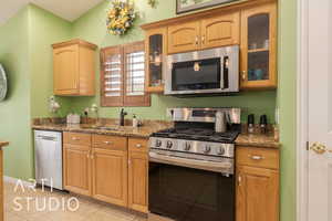 Kitchen featuring sink, dark stone countertops, stainless steel appliances, and light tile patterned flooring