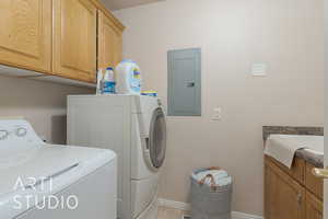 Washroom with washing machine and dryer, electric panel, light tile patterned floors, and cabinets