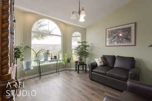 Living room featuring wood-type flooring, a textured ceiling, a chandelier, and vaulted ceiling