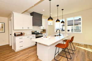 Kitchen with white cabinets, a kitchen bar, sink, stainless steel gas range oven, and a center island with sink