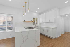 Kitchen featuring white cabinetry, hanging light fixtures, light hardwood / wood-style flooring, backsplash, and light stone counters