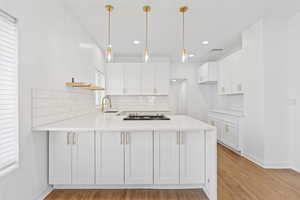 Kitchen featuring backsplash, white cabinetry, kitchen peninsula, and hanging light fixtures