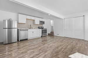 Kitchen with light hardwood / wood-style flooring, sink, backsplash, white cabinetry, and stainless steel appliances