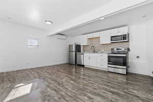 Kitchen featuring appliances with stainless steel finishes, backsplash, white cabinets, dark hardwood / wood-style floors, and a wall mounted AC