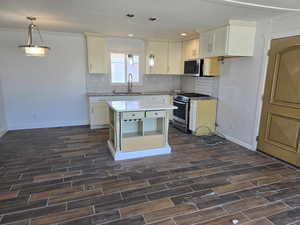 Kitchen with sink, white cabinetry, decorative light fixtures, appliances with stainless steel finishes, and a kitchen island