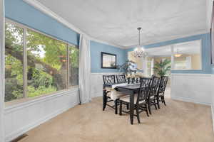 Carpeted dining space with crown molding, plenty of natural light, and an inviting chandelier