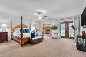 Carpeted bedroom with a stone fireplace, french doors, ceiling fan, and access to outside